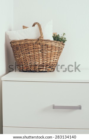 Wicker basket with a pillow and green home plant at the white wall on the chest of drawers, modern home interior decor