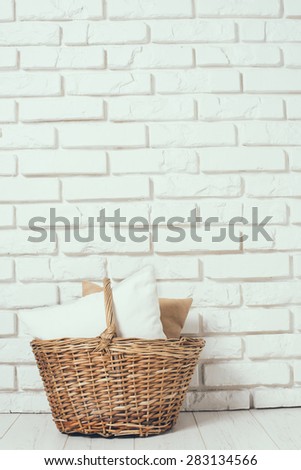 Wicker basket with a pillow at the white brick wall on the floor, rustic home interior decor with copy space
