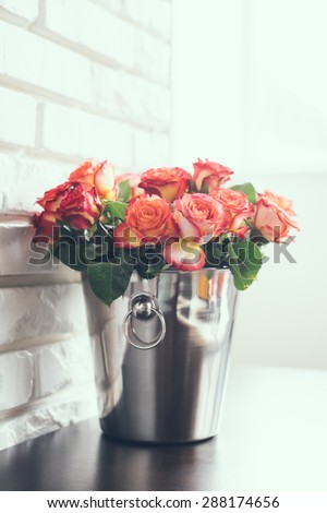 Bunch of fresh roses in a metal bucket for champagne on a table in a bright interior room