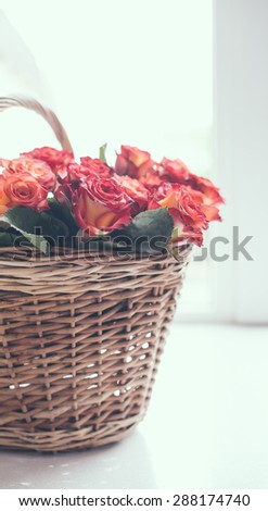 A bouquet of roses in a basket on the table in front of the window against backlight