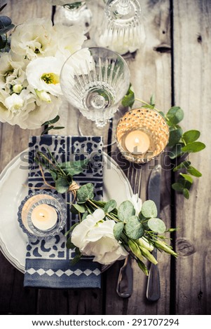 Table setting with white flowers, candles and glasses on old vintage rustic wooden table. Vintage summer wedding table decoration, top view.