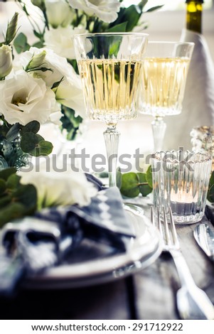 Table setting with white flowers, candles and glasses of champagne on an old vintage rustic wooden table. Vintage summer wedding table decoration.