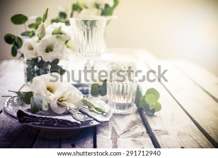 Table setting with white flowers, candles and glasses on old vintage rustic wooden table. Vintage summer wedding table decoration.