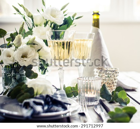 Table setting with white flowers, candles and glasses of champagne on an old vintage rustic wooden table. Vintage summer wedding table decoration.