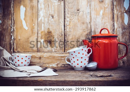 Vintage kitchen decor, red enamel coffee pot and cups with polka dots on an old wooden board background with copy space. Rustic home decor.