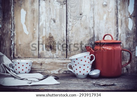 Vintage kitchen decor, red enamel coffee pot and cups with polka dots on an old wooden board background with copy space. Rustic home decor.