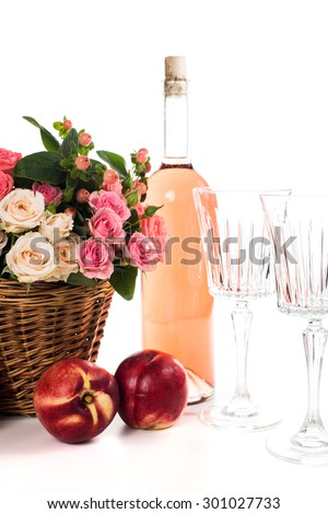 Fresh natural pink roses in a wicker basket  and a bottle of rose wine with two wineglasses and nectarines on white background isolated. Fruits, wine and flowers.