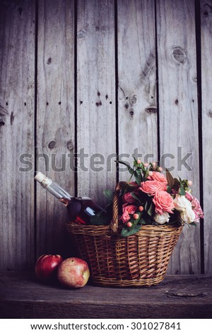 Rustic still life, fresh natural pink roses and a bottle of rose wine with nectarines in a wicker basket on an old wooden barn board background. Flowers and fruits for vintage wedding with copy space.