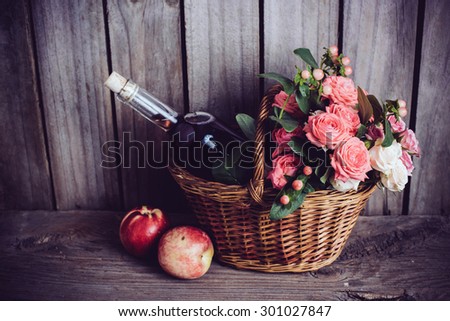 Rustic still life, fresh natural pink roses and a bottle of rose wine with nectarines in a wicker basket on an old wooden barn board background. Flowers and fruits for vintage wedding.