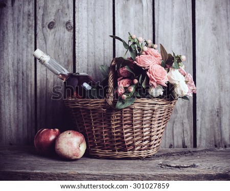 Rustic still life, fresh natural pink roses and a bottle of rose wine with nectarines in a wicker basket on an old wooden barn board background. Flowers and fruits for vintage wedding with copy space.