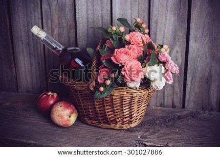 Rustic still life, fresh natural pink roses and a bottle of rose wine with nectarines in a wicker basket on an old wooden barn board background. Flowers and fruits for vintage wedding.