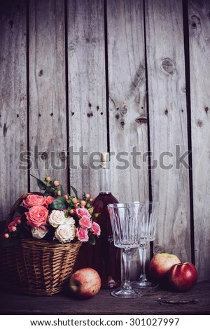 Rustic still life, fresh natural pink roses in a wicker basket  and a bottle of rose wine with two wineglasses and nectarines on an old wooden barn board background. Flowers and fruits for vintage