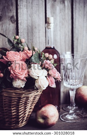 Rustic still life, fresh natural pink roses in a wicker basket  and a bottle of rose wine with two wineglasses and nectarines on an old wooden barn board background. Flowers and fruits for vintage