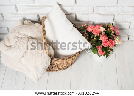 Bouquet of pink roses in vintage enamel coffee pot and basket with home textiles near the white brick wall. Cozy country home decor.