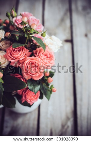 Bouquet of pink and beige roses in vintage enamel coffee pot on old wooden barn board background. Rustic flowers with copy space, closeup.