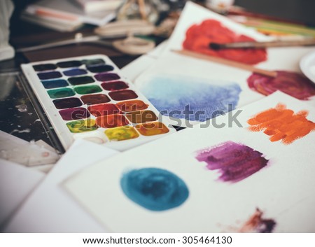 Mess in the the artist\'s studio, watercolor paints, brushes and sketches, palette and painting tools. Designer\'s working place, hipster style.