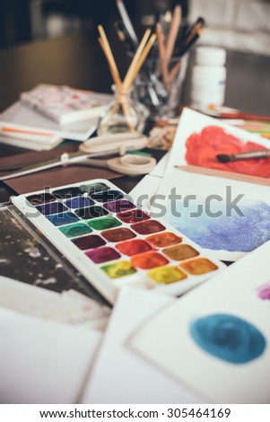 Mess in the the artist\'s studio, watercolor paints, brushes and sketches, palette and painting tools. Designer\'s working place, hipster style.