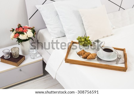 Breakfast in bed, tray with coffee, fruits and croissants on a bed with white linen in bedroom interior, hotel room