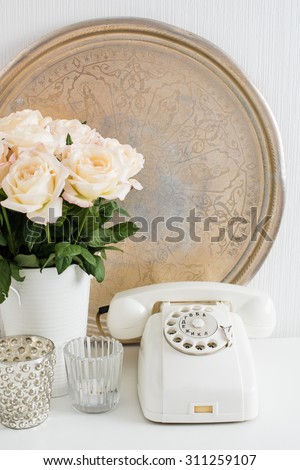 Vintage home interior decoration: white rotary phone, silver tray, candles and roses on a table. Apartment decoration retro style, closeup.