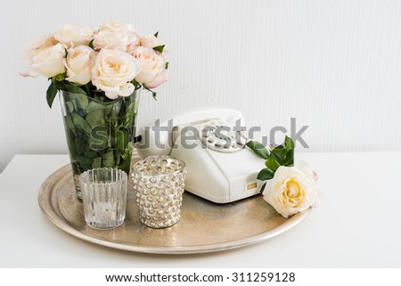Vintage home interior decoration: white rotary phone, silver tray, candles and roses on a table. Apartment decoration retro style, closeup.
