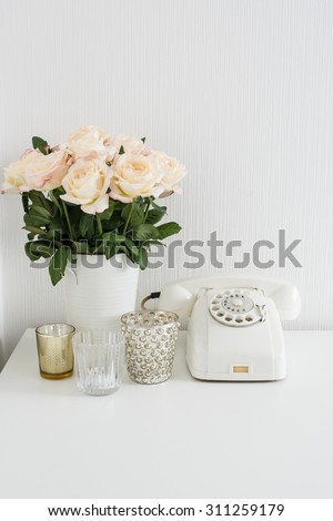 Modern interior decor with vintage details: white rotary phone and fresh flowers on a table. Clean white room in real apartment.