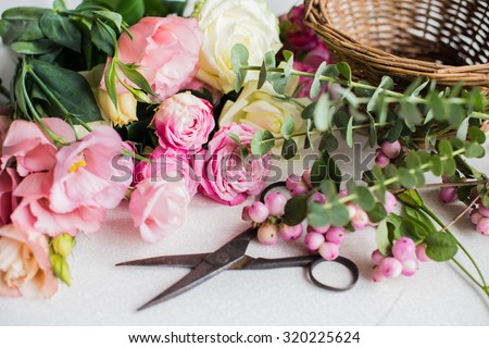Fresh flowers, leaves, and tools to create a bouquet on a table, florist's workplace.