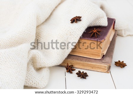 Winter still-life, old vintage books and knitted sweater on white painted wooden background.