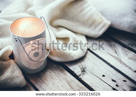 Cosy and soft winter background, knitted sweater and candles on an old vintage wooden board. Christmas holidays at home.