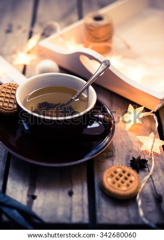 Winter holiday background: cup of tea, Christmas lights and other home decoration on vintage wooden table. Cozy holidays at home.