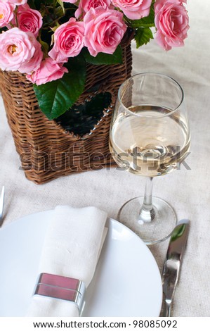 A glass of white wine and a basket of roses on the table
