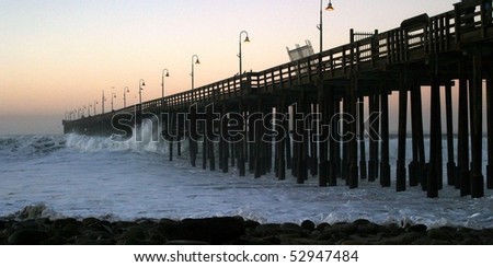 Ocean waves throughout at storm crashing into a wooden pier.
