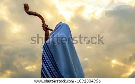 Blowing  the shofar for the Feast of Trumpets - Jewish man in a tallit prayer shawl against dramatic sky
