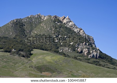 A green, rolling hillside with massive rock outcroppings against a bright, blue sky.