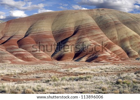 Horizontal landscape of the colorful Painted Hills in Oregon against cloudy blue skies.