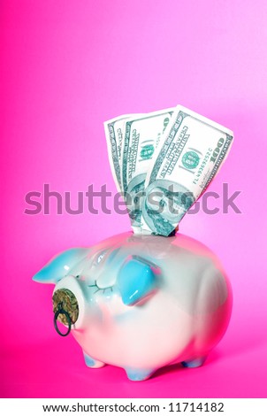Vertical image of a piggy bank with US currency sticking out of the coin slot, all against a pink background.