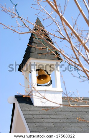 Vertical image of a bell tower and its gold bell through tree branches against a blue sky.