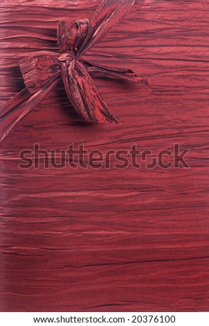 Vertical crimson red fabric textured gift background with a ribbon and box in the upper left corner running diagonally.