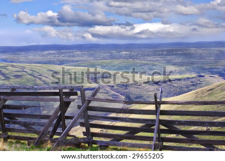 Horizontal landscape of eastern Oregon south of Pilot Rock with an old wooden snow fence in the foreground and blue cloudy skies in the background.