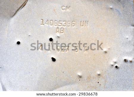 Gray, grungy piece of old metal with random numbers and letters, riddles with bullet holes.