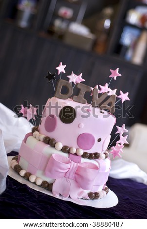 A pink fondant cake with Diva and stars topping it featured in a bakery.  Shallow DOF with focus on the front of the cake.