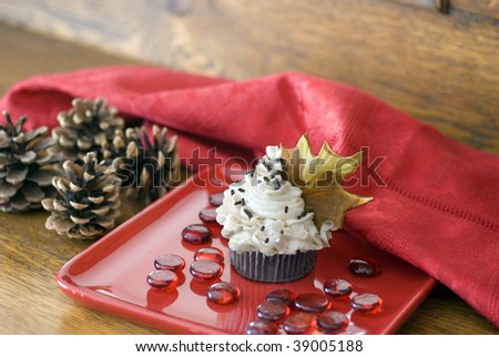 An autumn themed chocolate cupcake with a brown fondant maple leaf garnish on a red dessert plate.
