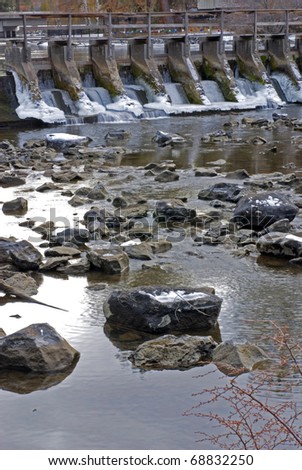 An ice and snow covered dam and a low-water river with river rocks showing during winter.