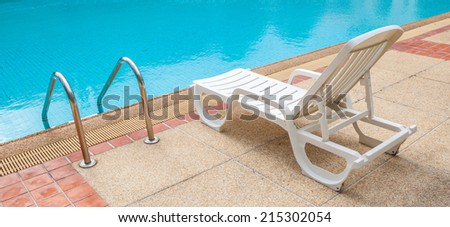 White lounge chair at the pool side near ladder; blue swimming pool