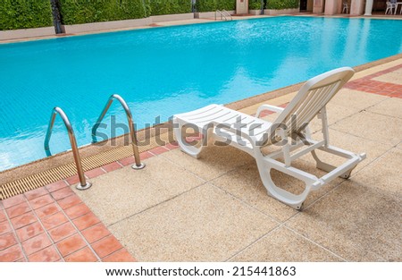 White lounge chair at the pool side near ladder, blue swimming pool