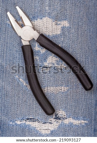Pliers black handle tool with lots of torn blue jeans pattern background, concept for fixing and useful maintenance.