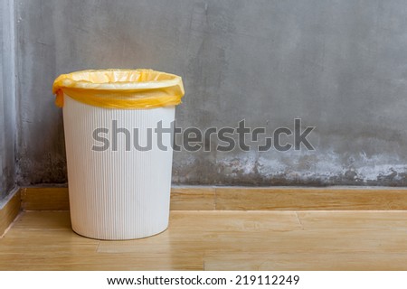 The white plastic bin with orange bag on wooden floor with exposed cement background, for cleaning and recycle.
