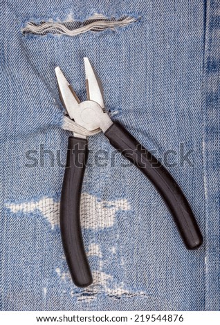 Pliers black handle tool with torn blue jeans pattern background, concept for fixing and useful maintenance.