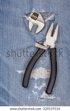 2 types of pliers black handle tool pierce through old blue jeans background, concept for fixing and useful maintenance.