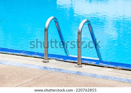A view of a light clear blue swimming pool with steel ladder, outdoor swimming pool.