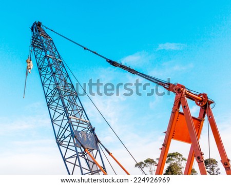 The grunge construction crane for heavy lifting is working in construction site and clear blue sky day.